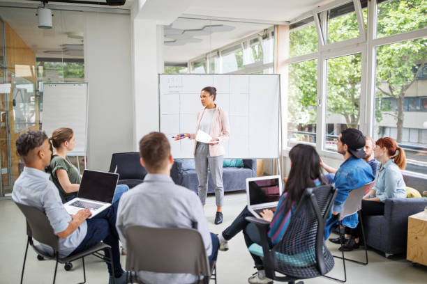 Businesswoman giving presentation to team Businesswoman giving presentation to team sitting in conference room. Female business manager explaining new business strategies to team. digital marketing meetings stock pictures, royalty-free photos & images